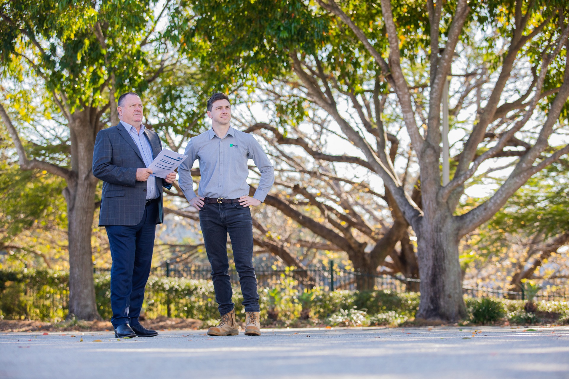 two men standing next to each other in front of trees